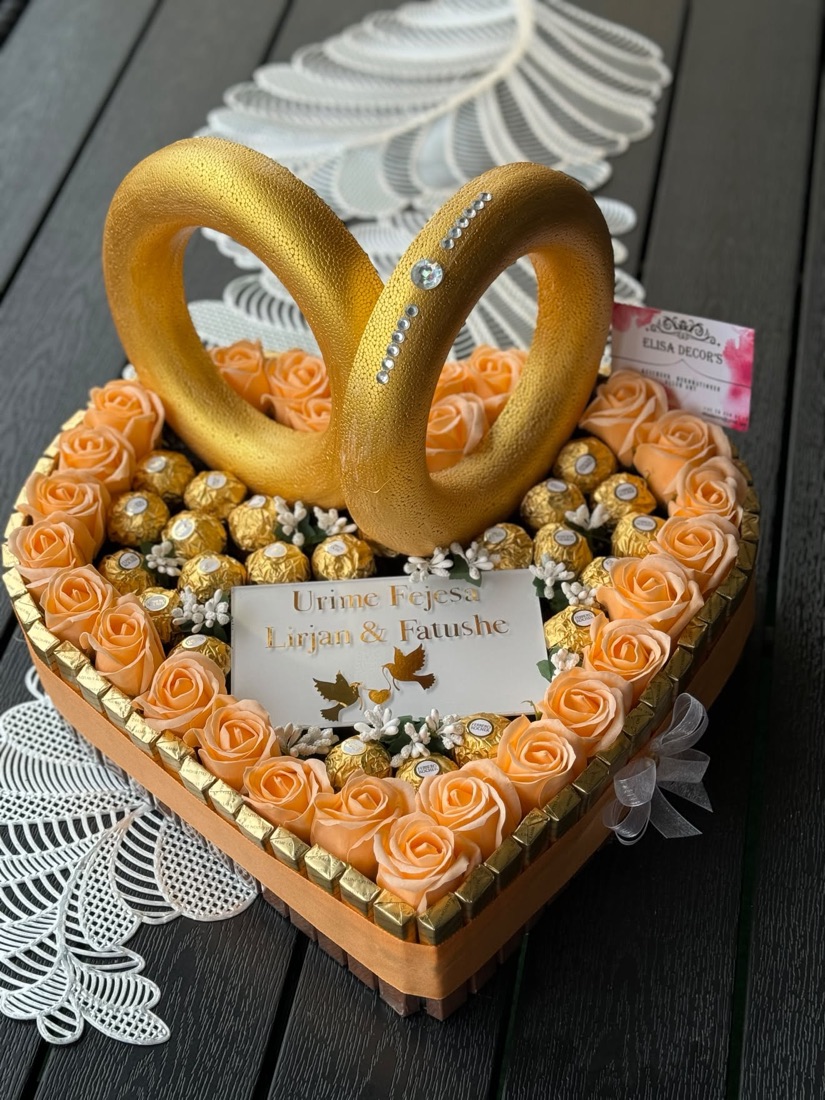 Herz aus orangen Rosen und Pralinen mit zwei goldenen Ringen